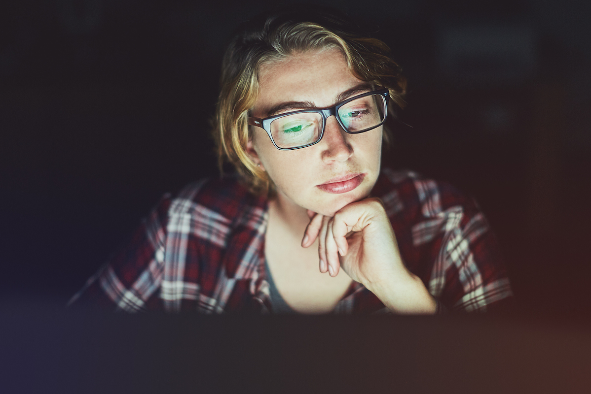 Une jeune femme avec des lunettes qui regarde attentivement son écran d'ordinateur en soirée